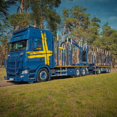 Blue truck with DOLL flatbed trailer on a sunny country road during loading.