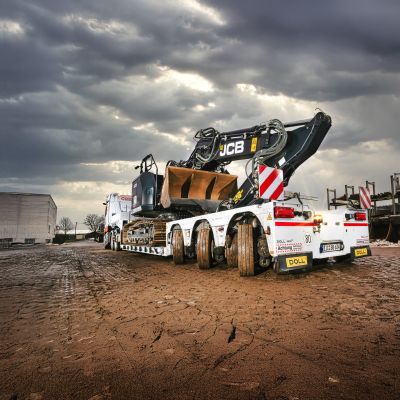 Excavator parked on a low loader for heavy transport under a dramatic sky.