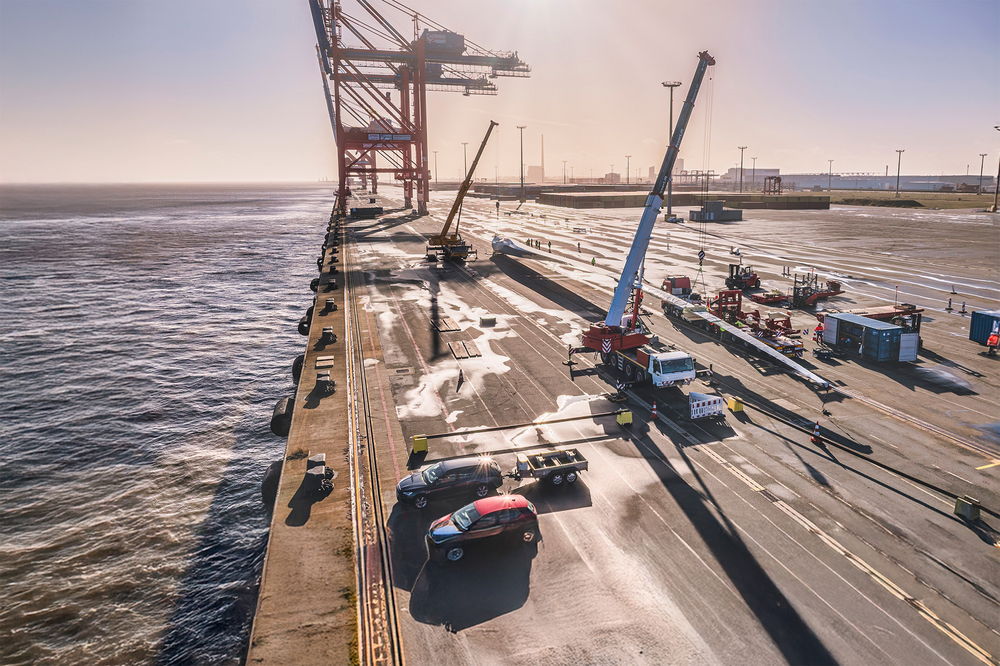 Transport lourd de pales d'éoliennes avec des grues au port au coucher du soleil