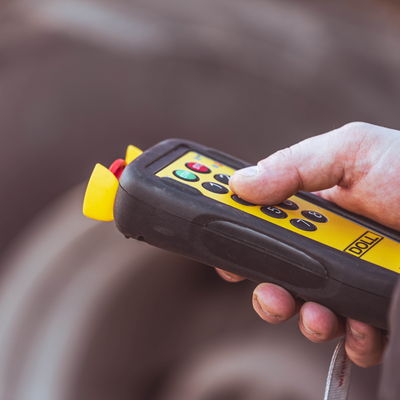 Gros plan sur une main tenant une télécommande jaune et noire de DOLL pour piloter un véhicule de transport lourd.